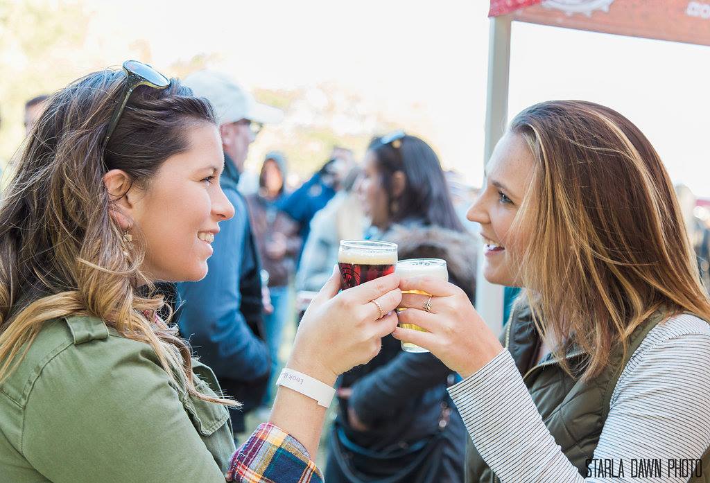 Two women cheersing with glasses of beer at an outdoor event.