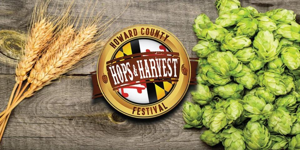 Logo for the Howard County Hops & Harvest Festival, flanked by stalks of wheat on the left and fresh hop cones on the right, on a wood grain background.