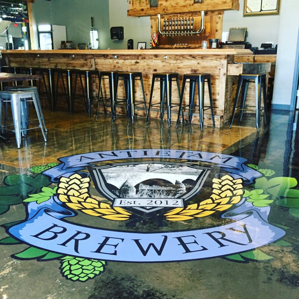 Antietam Brewery logo painted on a concrete floor in front of a wooden bar with stools.
