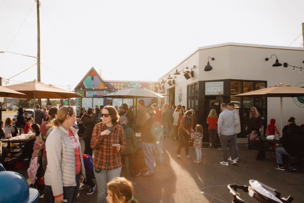 A crowded outdoor patio at a brewery with patrons gathered at tables and near the building entrance.