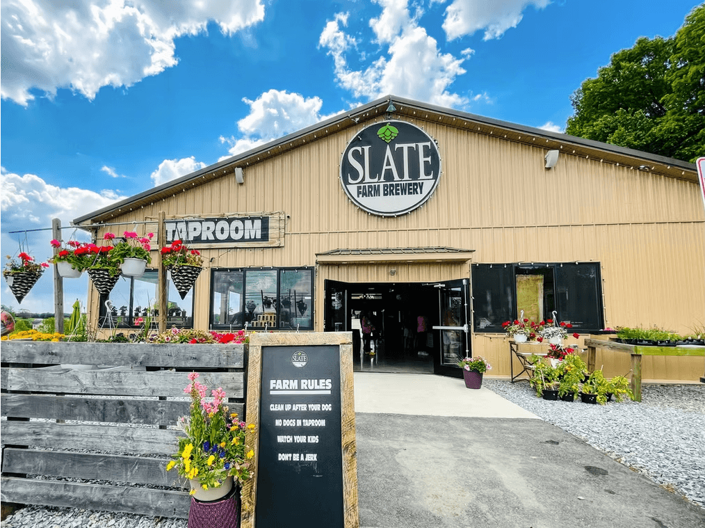 The exterior of Slate Farm Brewery featuring a taproom entrance and a sign listing “Farm Rules.”