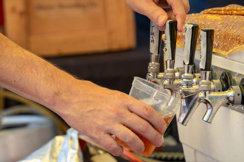 A hand filling a clear plastic cup from a beer tap handle.